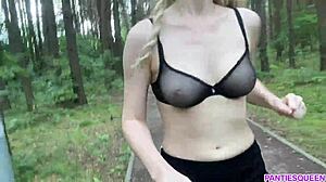 Blondinka telovadi na prostem v parku, razkriva svoje golo telo in poskakujoče prsi